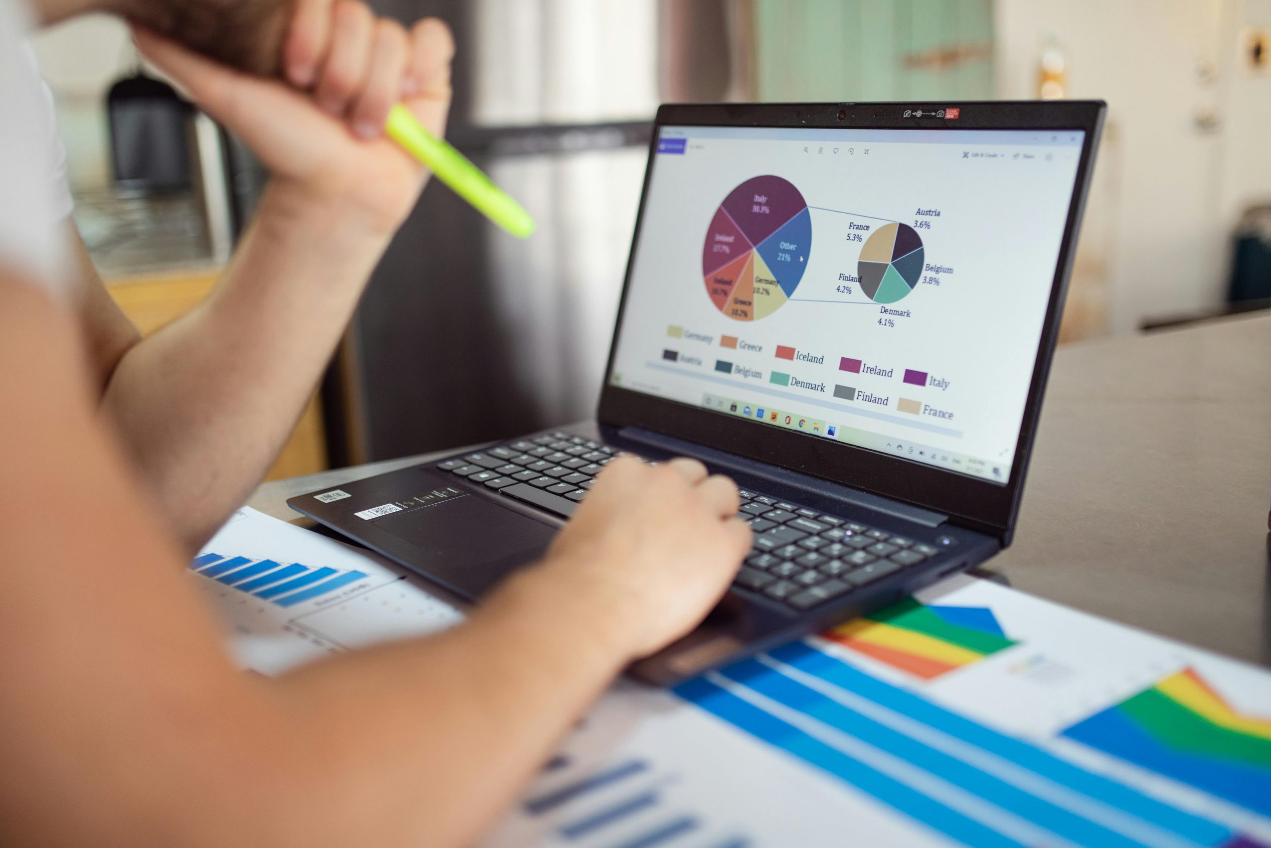 About Person analyzing financial charts and graphs on a laptop with colorful documents, showcasing market analysis.